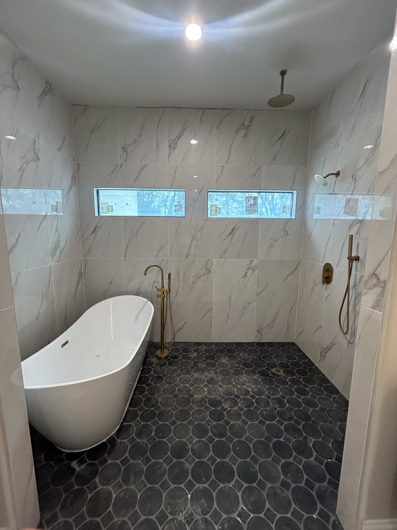 Completed luxury bathroom with marble tile, freestanding tub, and brass fixtures